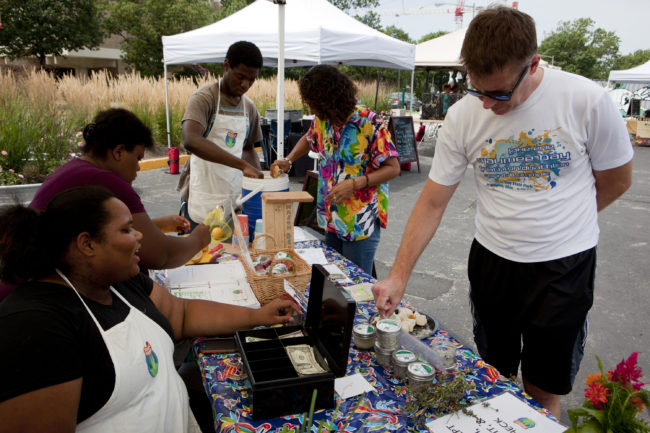 Roshawn Little (left) invites customer Nate Kohring to try the herbed salt with bread at the Aya farmers market on Saturday. Lydia Thompson/NPR