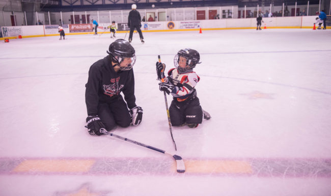 Juneau Bantam standout Greyson Liebelt works one-on-one with Jacob King who is getting his first taste of hockey at Treadwell Ice Arena. (Photo by Steve Quinn)