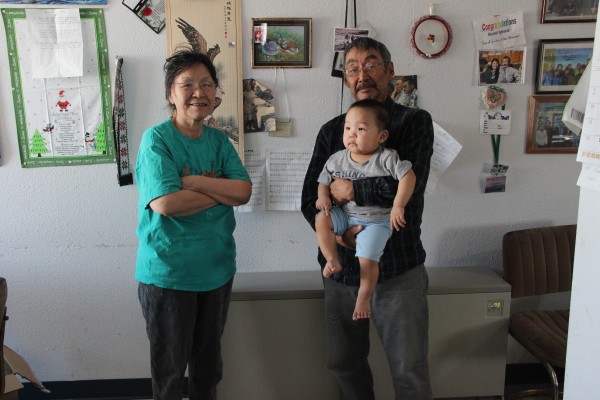 Chaninik Wind Group founder William Igkurak with his wife Rachel and grandson Ty, standing in front of one of the system’s electric thermal stoves. (Photo by Rachel Waldholz/APRN)