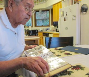 Musician Fred John looks through a photo album of old pictures from his time traveling and singing with a church group. (Photo by Leila Kheiry/KRBD)