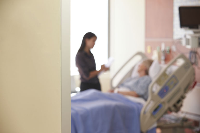 Focus On Hospital Room Sign With Doctor Talking To Patient. Photo from Kaiser Health News.