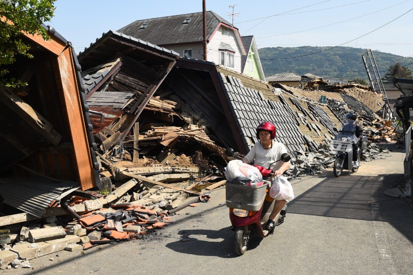 A woman rides a scooter in front of a collapsed house on Friday in Mashiki, Kumamoto, Japan, after a 6.2 magnitude earthquake struck the region Thursday. Another strong quake, preliminary magnitude of 7.0, struck the same area early Saturday morning local time. (Masterpress/Getty Images)
