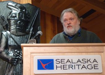 The Alaska State Museum's Steve Henrickson discusses Tlingit armor during a Dec. 1, 2016, lecture at the Walter Soboleff Building. To the left, Preston Singletary's house pole depicts an armored warrior. (Photo by Ed Schoenfeld/CoastAlaska News)