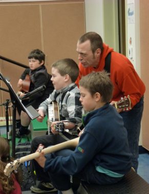 Patrick Murphy works with banjo and guitar players Quinn Andel, Eric Holberg and Andrew William during a class at Gastineau Elementary School. (Photo by Ed Schoenfeld/CoastAlaska News)