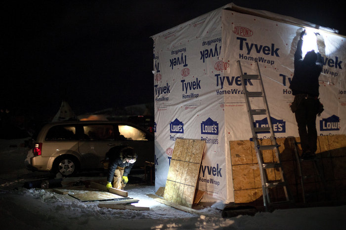 Volunteers wrap insulation around a small box bunkhouse, one of many winterized structures popping up in the three camps along the Cannonball River. Celia Talbot Tobin for NPR