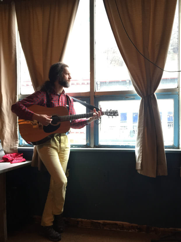 Juneau songwriter George Kuhar stands in the window of Peabody's Monster, a downtown rehearsal space and musician cooperative. He performs at 8:00 Tuesday night at the Alaska Folk Festival. (Photo by Jack Sanders/KTOO)