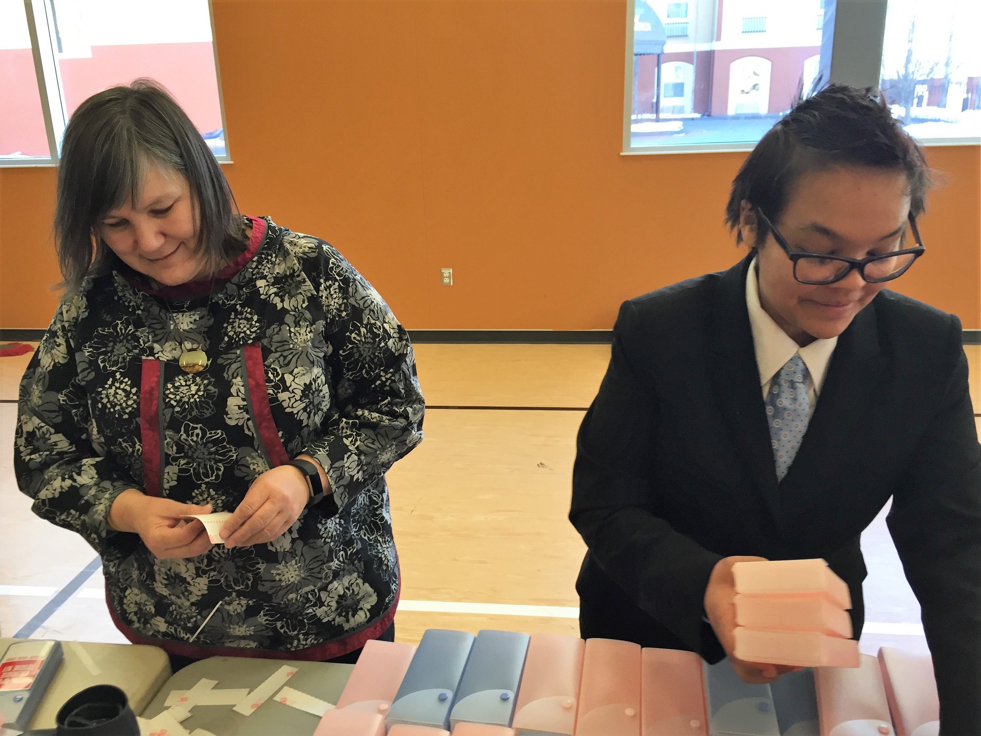Department of Health and Social Services Commissioner Valerie “Nurr’araaluk” Davidson and Nichelle Willams pulls stickers off boxes with on a Narcan kit assembly line at Covenant House in March. (Photo by Anne Hillman/Alaska Public Media)