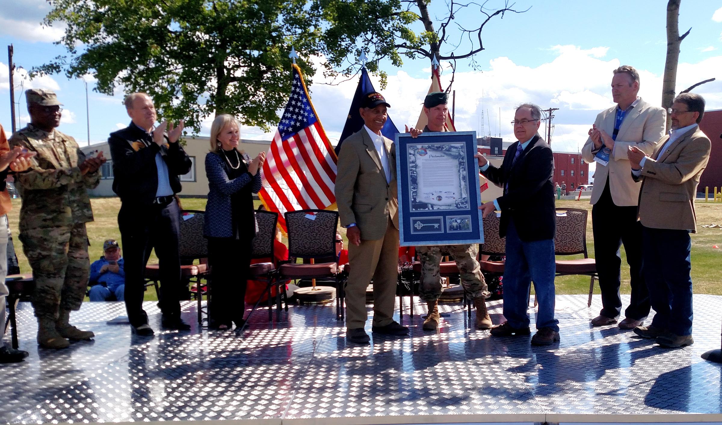 Fort Greely senior officers and invited dignitaries applaud after Leonard Larkins receives a proclamation and key to the city of Delta Junction at the end of Saturday's ceremony on Fort Greely. From left, Chaplain Maj. Ernest Ibanga, Gov. Bill Walker, First Lady Donna Walker, Larkins, Greely Garrison Commander Lt. Col. Michael Foote, Delta Mayor Pete Hallgren, state Sen. Mike Dunleavy and state Rep. George Rauscher. (Photo by Tim Ellis/KUAC)
