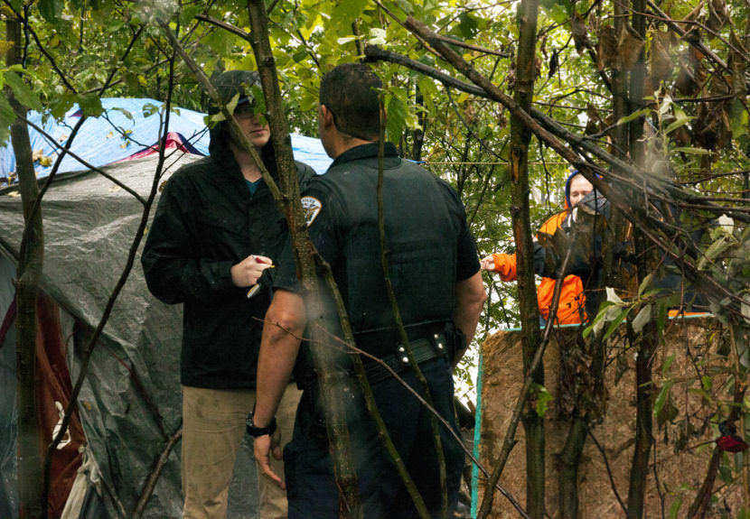 Juneau Empire reporter interviews a Juneau police officer Tuesday, August 22, 2017, at an encampment on Alaska Mental Health Trust property off Egan Drive. Juneau police served a notice of trespass to the encampment. The notice gave the encampment two weeks to leave the property. (Photo by Tripp J Crouse/KTOO)