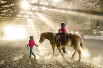 Sunlight streams into the dusty barn as Higgins carries another rider around the arena.
