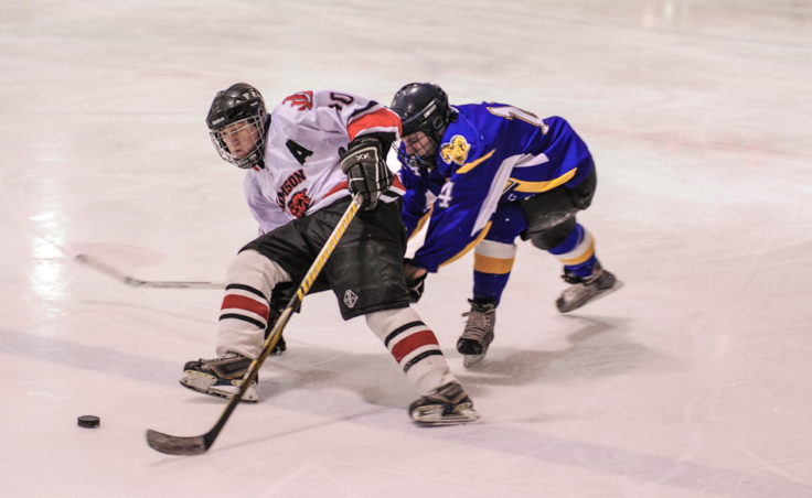 Juneau’s Ethan Seid hangs on to his balance and the puck while being trailed by Monroe Catholic’s Garrett Grahek.