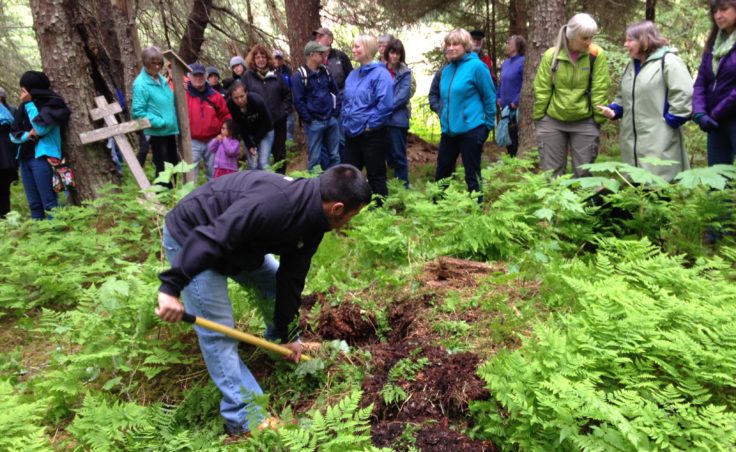 Martin Stepetin digs a hole for the Atka memorial plaque. Onlookers are those who also joined the Friends of Admiralty Island tour. (Photo by Lisa Phu/KTOO)