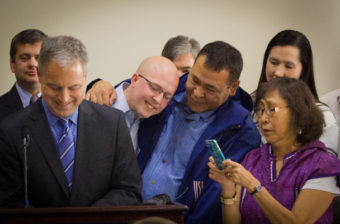 Representative Jonathan Kreiss-Tomkins of Sitka, Nome’s Bernadette Yaayuk Alvanna-Stimpfle, and others look on as Gov. Sean Parnell signs the bill into law. (Photo by Matthew F. Smith/KNOM)