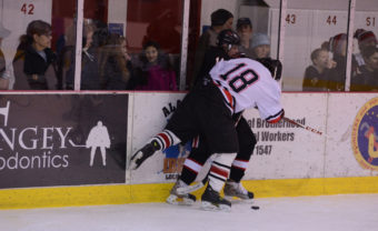 Juneau’s Niko Hebert pins Houston’s Isaac Smoldon against the boards during Friday’s game at Treadwell Ice Arena.