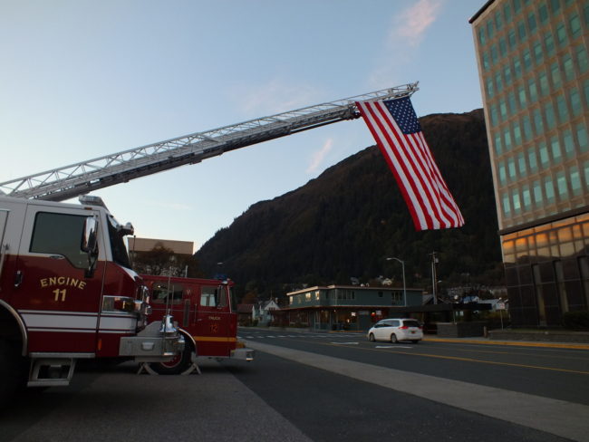 Station 1 vehicles are pulled out of the station with a large Amercian flag hanging over Glacier Avenue. (Photo by Matt Miller/KTOO)