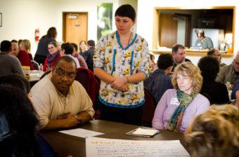 Darlene Trigg (standing) with the First Alaskans Institute listens in on a roundtable discussion with Alaska Dept. of Corrections Commissioner Ron Taylor and Kari van Delden with University of Alaska-Fairbanks’ Cooperative Extension Service. (Photo by Matthew F. Smith/KNOM)
