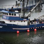A crewmember on the Trinity throws a floral wreath into the water in front of the Alaska Commercial Fishermen's Memorial. More than a hundred people gathered May 7, 2016 for the Blessing of the Fleet in Juneau. (Photo by Jennifer Canfield/KTOO)
