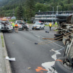 2 tow trucks work to upright an overturned flatbed truck on Egan Drive on July 25th, 2016. (Photo by Mikko Wilson / KTOO)