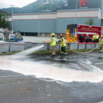 Firefighter Krista Telnes and Captain Todd Cameron of Capital City Fire/Rescue wash salmon slime from Egan Drive after a truck rollover on July 25th, 2016. (Photo by Mikko Wilson / KTOO)