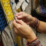 Clarissa Rizal's fingers dexterously manipulate the various colors of yarn Monday afternoon, August 22, 2016, as she works on the side borders of the Weavers Across Waters Chilkat/Ravenstail community robe. Rizal estimates that it takes her an hour to weave one inch of the side border, which means the robe is incredibly time intensive. (Photo by Tripp J Crouse/KTOO)