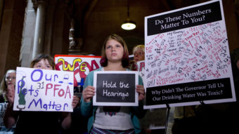 Protesters in Hoosick Falls, N.Y., in June hold signs calling for hearings on contamination in their town's drinking water by a chemical related to firefighting foam. Mike Groll/AP