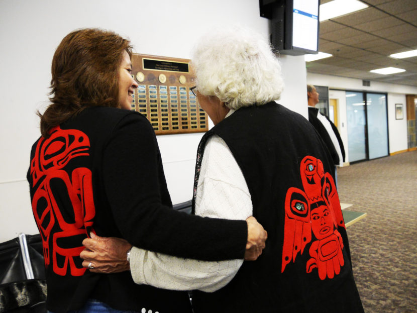(From L to R) Valerie Hillman shows off her clan's crest, the T'akdeintaan's Raven, while holding arms with Hoonah tribal elder Lillian Austin, who's clan crest is the Shangukeidí's Thunderbird. (Photo by Lakeidra Chavis/ KTOO)