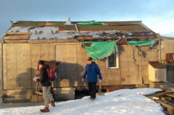 Mayor Myron Kingeekuk and a Red Cross employee survey storm-damaged homes in the community. (Photo by Davis Hovey/KNOM)