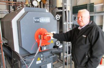 Airport Manager Mike Carney stands next to the Ketchikan International Airport’s new biomass wood-pellet boiler last summer. (File photo by Leila Kheiry/KRBD)