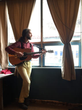 Juneau songwriter George Kuhar stands in the window of Peabody's Monster, a downtown rehearsal space and musician cooperative. He performs at 8:00 Tuesday night at the Alaska Folk Festival. (Photo by Jack Sanders/KTOO)