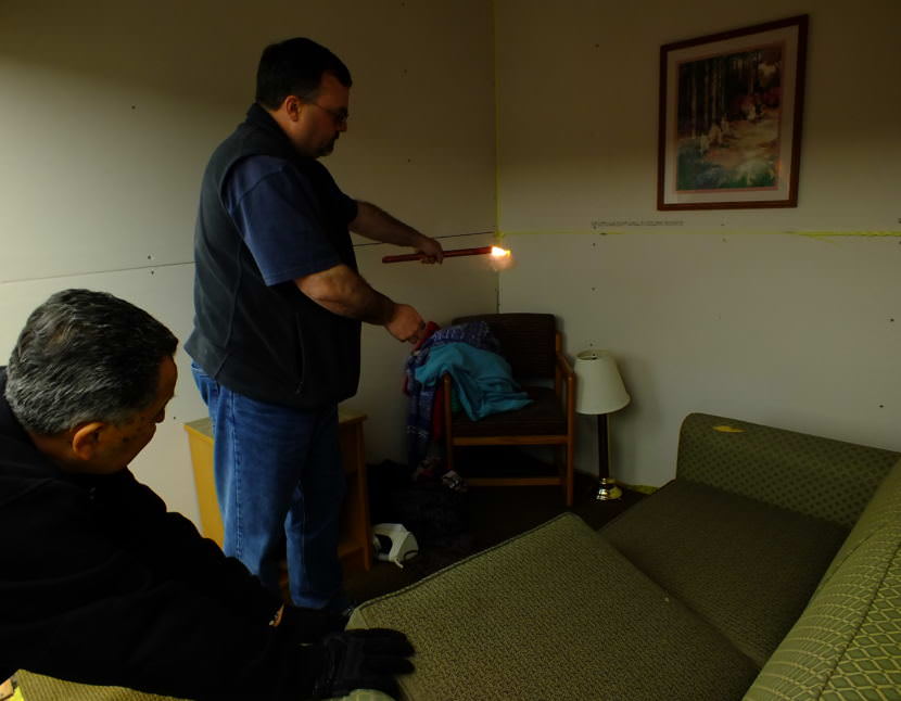 Instructor John Gamboa (bottom left) assists instructor Brian Balega as he ignites a fire one of the staged rooms during a recent fire investigator training exercise at Juneau’s Hagevig Regional Fire Training Center. (Photo by Matt Miller/KTOO)