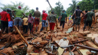 Sri Lankan military rescuers and villagers stand on the debris of a house that was destroyed in a landslide in the village of Bellana, in the Kalutara district of Sri Lanka, on Friday. Mudslides and floods triggered by heavy monsoon rains have killed scores of people in the island nation.