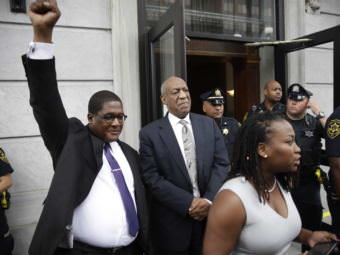 Bill Cosby looks on as spokesman Andrew Wyatt triumphantly raises his fist outside the Montgomery County Courthouse in Norristown, Pa., on Saturday. Cosby's legal and publicity team treated the mistrial as a victory, though prosecutors immediately said they plan to retry the case.