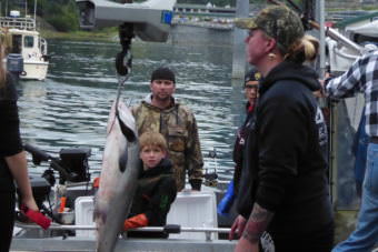 A family watches from their boat as Kami Bartness weighs one of their fish on a hanging scale at a float in the Auke Bay harbor.