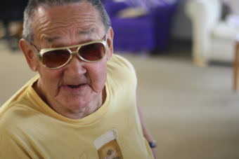Paul “Elvis” Chythlook dons a pair of gold chrome shades at the piano bench. He plays for the community in the Dillingham Senior Center regularly, gospel and traditional tunes he knows by heart. (Photo by Zoey Laird/KDLG)