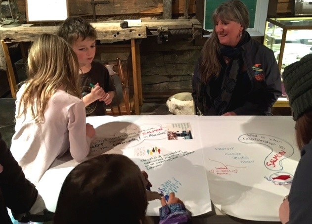 Kitty Farnham, right, watches children write responses to fisheries-based questions. (Photo by Kayla Desroches/KMXT)