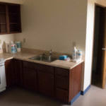 A small kitchenette in the corner of an apartment with a full sized refrigerator, oven, and sink