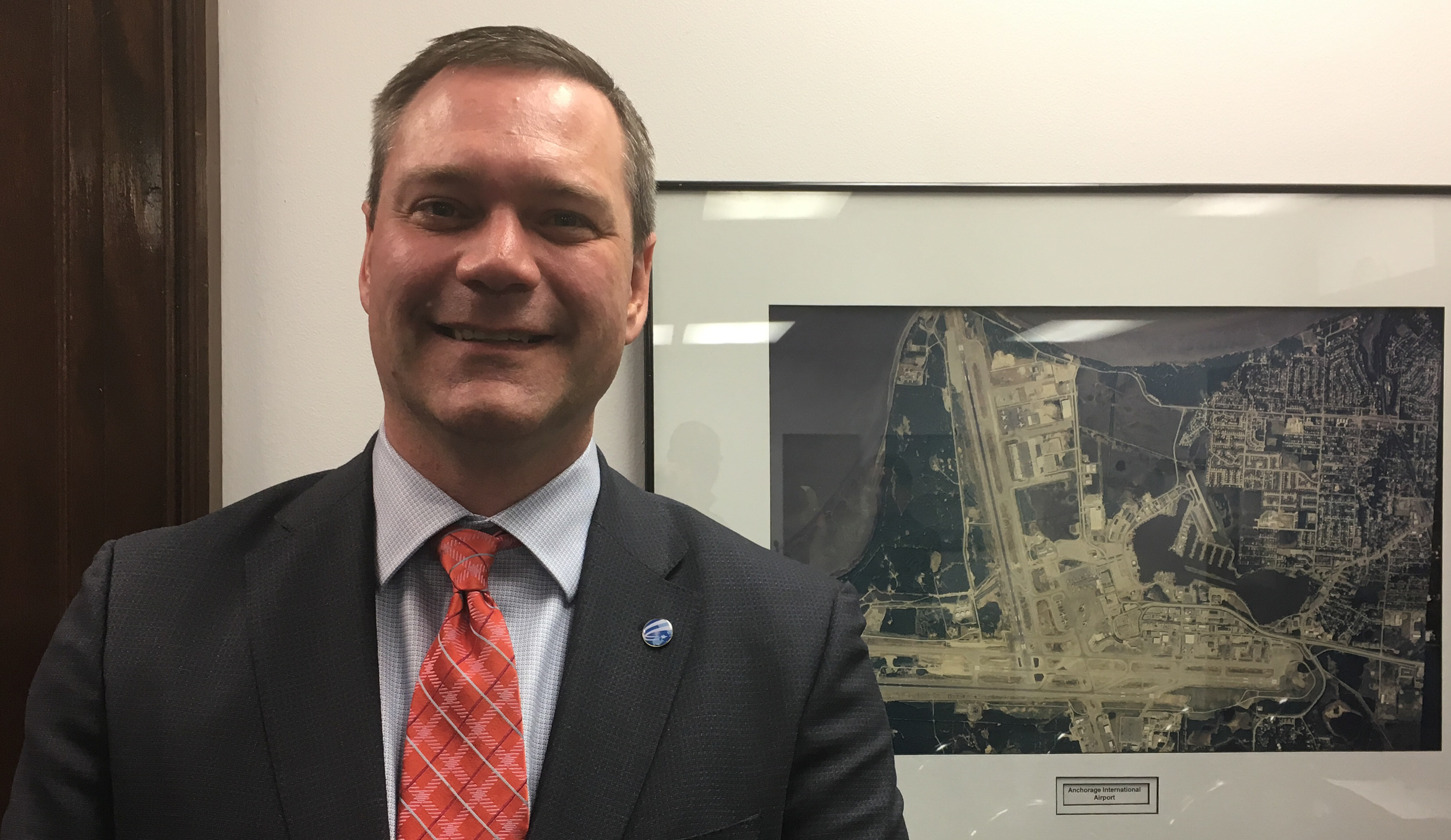 Ted Stevens Anchorage International Airport general manager Jim Szczesniak stands in front of a photo of the airport, Feb. 20, 2018. He said he would like to see the airport build on its role in global cargo transport. (Photo by Andrew Kitchenman/KTOO)