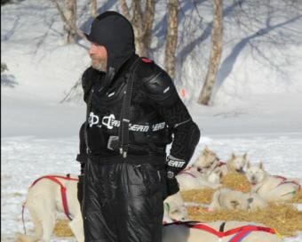 Jim Lanier handling his dogs at the Finger Lake checkpoint in his protective mountain biking gear. (Photo by Zachariah Hughes/Alaska Public Media)