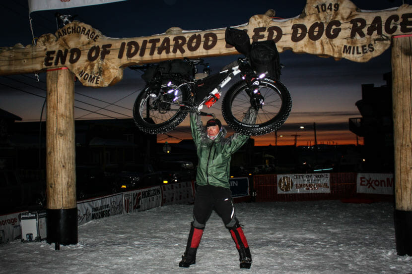 Jay Petervary of Idaho hoists his fat-tire bike under the burled arch in Nome after winning the 2015 Iditarod Trail Invitational. He had his fourth finish and third win on March 14, 2018, with a time of 16 days, 23 hours and 45 minutes.