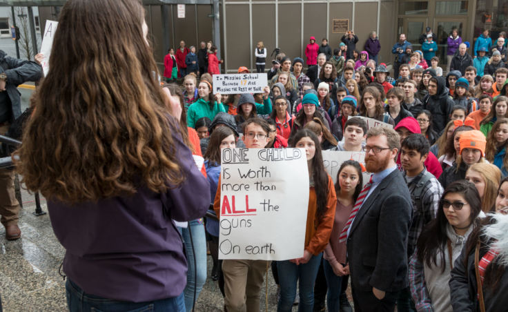 Katie McKenna speaks on the steps of the Alaska State Capitol building in Juneau at a student walkout protest on Wednesday, March 14, 2018. Students and Juneau Rep. Justin Parish, wearing the coat and tie, listen.