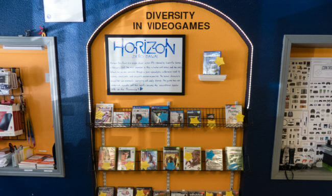 An orange archway alcove inlaid into a wall. A sign reading "Diversity in Videogames" sits over shelves of video game boxes.