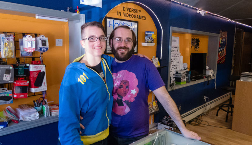 A portrait of Emry and Casey Harris behind the counter of the Game On store