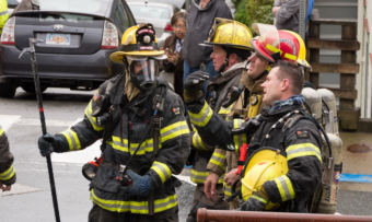 A group of firefighters talk at the corner of Fifth and Franklin streets after the house fire there on May 28, 2018. (Photo by David Purdy/KTOO)