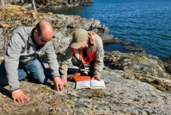 Museum archaeologist Patrick Saltonstall and helicopter pilot Keller Wattum document a petroglyph site on Afognak. (Photo courtesy Patrick Saltonstall)