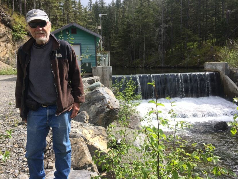Jim Macovjak is part of an ad hoc group that calls themselves the Power Rangers. He stands if front of the dam and intake for the Falls Creek Hydroelectric Project. A 30-inch pipe beneath him transports water to the generator. The dam itself is constructed of variable-size bladders that can adjust water flow. (Photo by Scott Burton/KTOO)