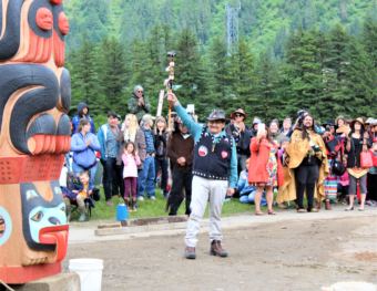 John Morris, a member of the Yanyeidí clan who once called the site home, raises his arm in triumph after helping to install the Gooch (wolf) totem pole. June 6, 2018. (Photo by Adelyn Baxter/KTOO)