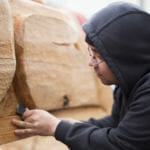 Artist Sam Sheakley helps finish the 40 foot Yanyeidí totem pole at Harborview Elementary School on May 29, 2018. (Photo by Annie Bartholomew/KTOO)