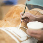Merritt Johnson paints Chilkat designs onto the 40 foot Yanyeidí totem pole at Harborview Elementary School on May 29, 2018. (Photo by Annie Bartholomew/KTOO)