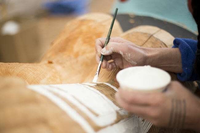 Merritt Johnson paints Chilkat designs onto the 40 foot Yanyeidí totem pole at Harborview Elementary School on May 29, 2018. (Photo by Annie Bartholomew/KTOO)