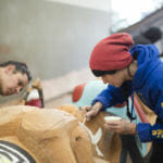 Indigenous artist Merritt Johnson works alongside her partner Nicholas Galanin painting the 40 foot Yanyeidí totem pole at Harborview Elementary School on May 29, 2018. (Photo by Annie Bartholomew/KTOO)